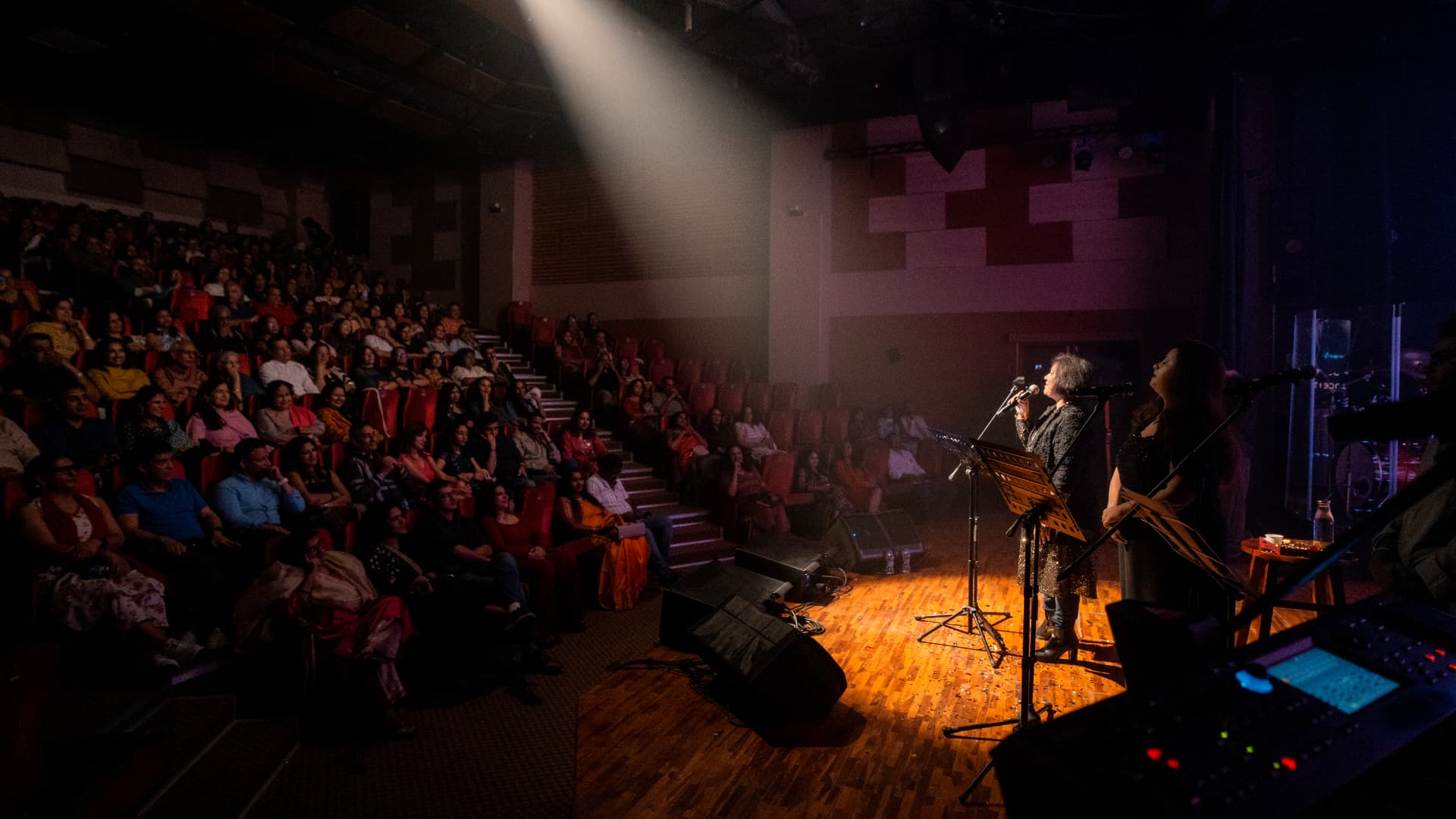 A spotlit stage before a full auditorium at The Jugni Concert